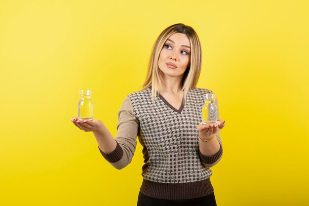 Portrait of beautiful blonde woman holding two glasses of still water. 