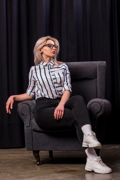 Portrait of a beautiful blonde young woman sitting on armchair with his crossed legs