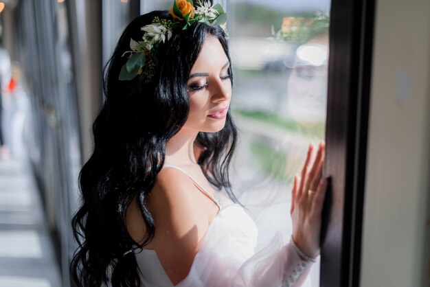 Portrait of beautiful brunette bride with closed eyes near the window on a beautiful sunny day