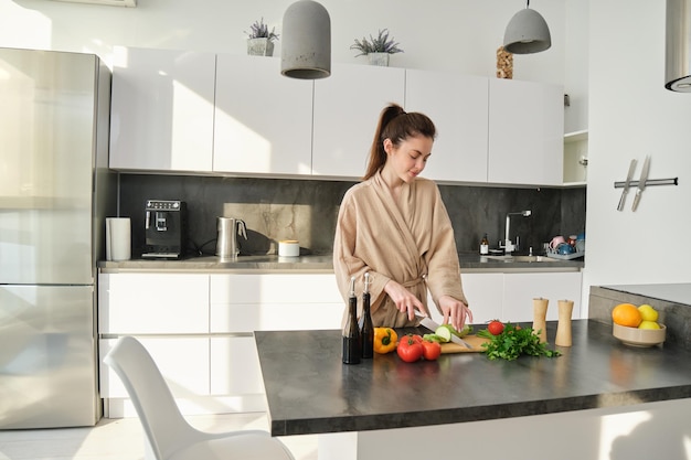 Foto gratuita ritratto di bella ragazza castana che taglia le verdure per il pasto che prepara insalata nel mangiare della cucina