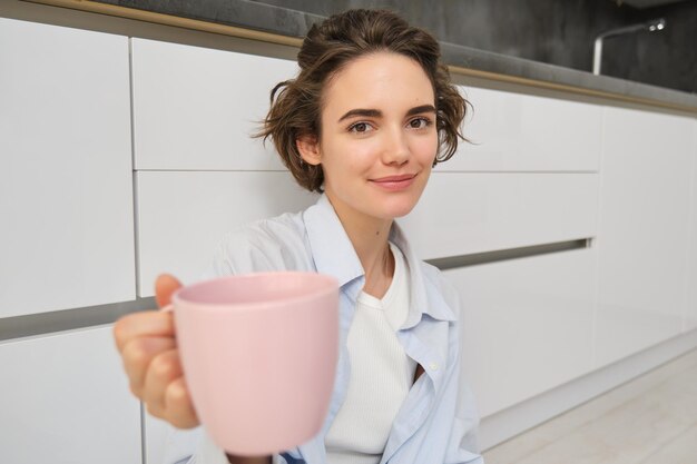아름다운 브루네트 소녀의 초상화는 커피나 차를 머그잔에 담아 그녀와 함께 마차를 마실 것을 제안합니다