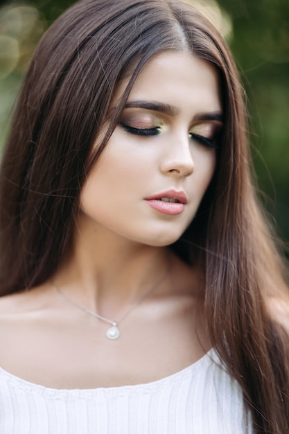 Portrait of a beautiful brunette girl with green eyes In a city park on a green background Closeup