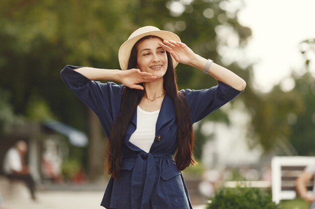 Portrait of beautiful brunette. Model in summer city. Woman in a straw hat.