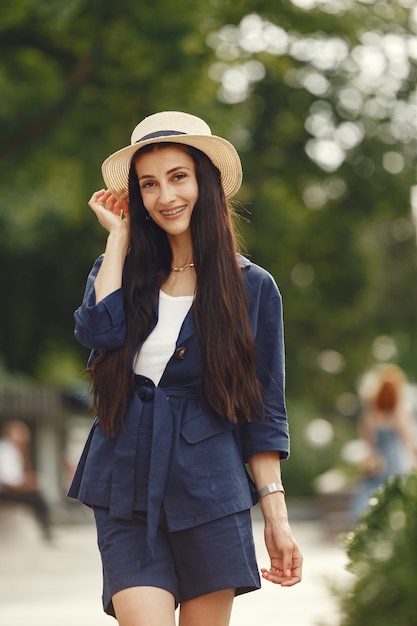 Portrait of beautiful brunette. Model in summer city. Woman in a straw hat.