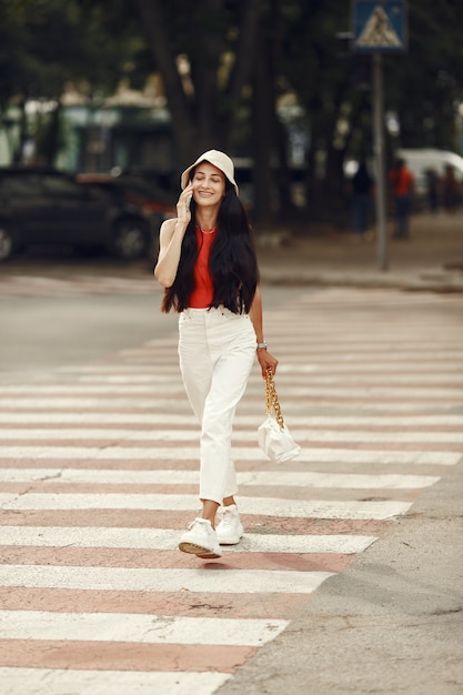 Portrait of beautiful brunette. Model in summer city. Woman walks with mobile phone.