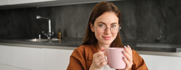 Free photo portrait of beautiful brunette woman enjoys time at home drinks coffee from her pink mug sits in