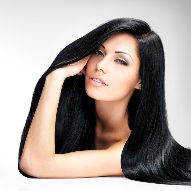 Portrait of a beautiful brunette woman with long straight hair poses at grey