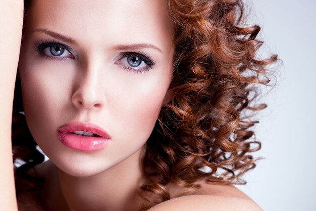 Portrait of beautiful brunette young woman with bright make up. Closeup face with curly hairstyle.