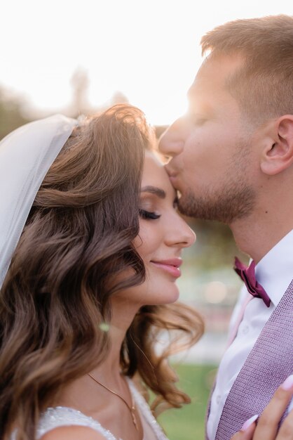 Portrait of beautiful caucasian bride and groom outdoors with closed eyes, kissing