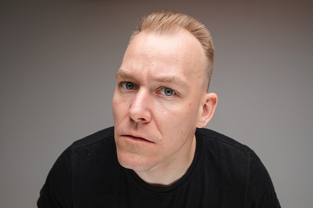 Portrait of beautiful caucasian male in black t-shirt and tries to see something, picture isolated on grey wall