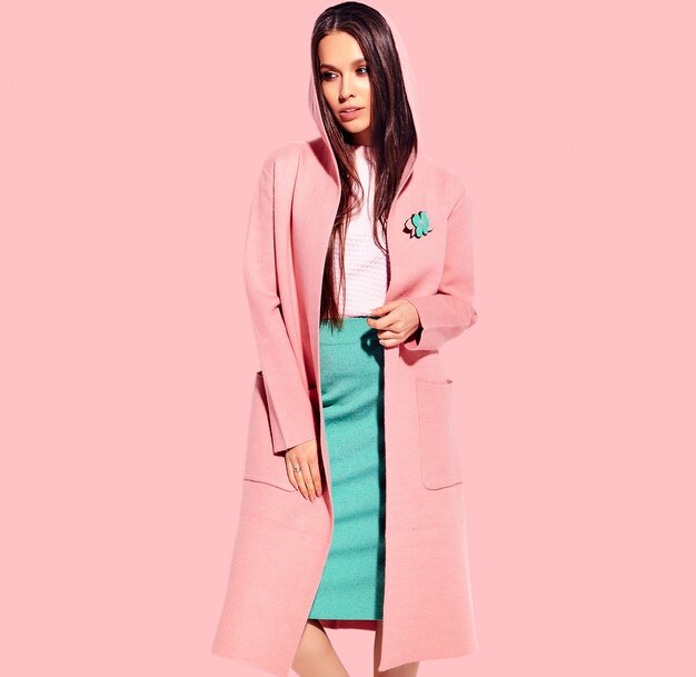 Portrait of beautiful caucasian smiling brunette woman model in bright overcoat and summer stylish skirt posing  on pink background