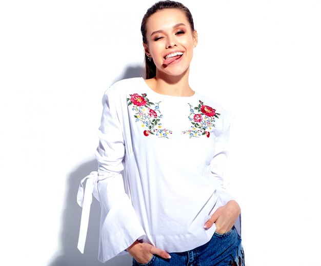 Portrait of beautiful caucasian smiling brunette woman model in white blouse and summer stylish blue jeans with flowers print