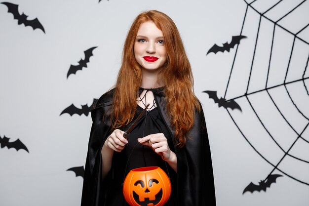 Portrait of beautiful caucasian witch holding orange pumpkin for celebrating halloween.