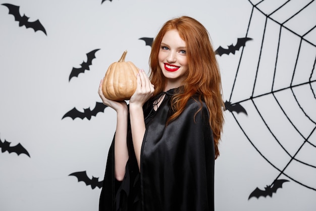 Portrait of beautiful caucasian witch holding pumpkin for celebrating halloween.