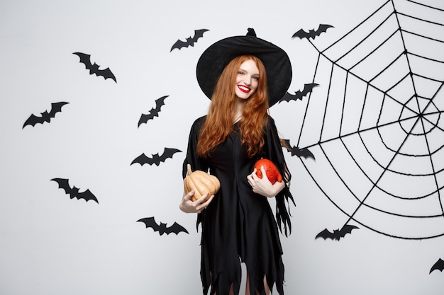 Portrait of beautiful caucasian witch holding pumpkin for celebrating halloween