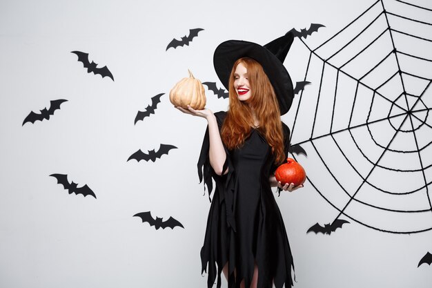 Portrait of beautiful caucasian witch holding pumpkin for celebrating halloween