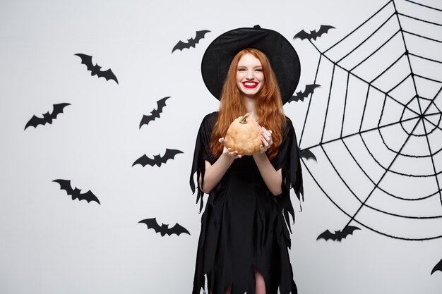 Portrait of beautiful caucasian witch holding pumpkin for celebrating halloween