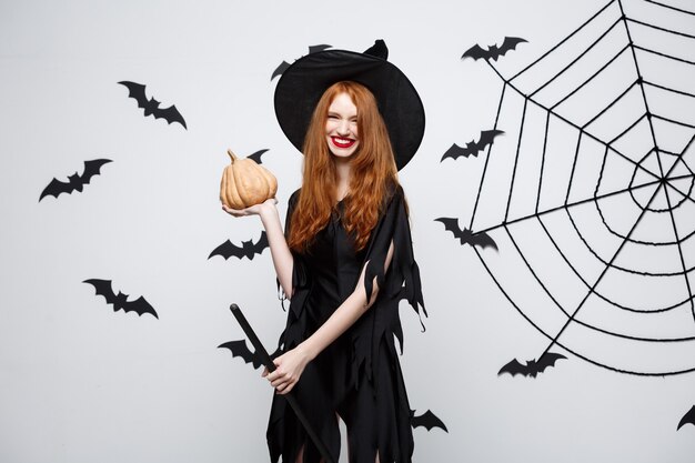 Portrait of beautiful caucasian witch holding pumpkin for celebrating halloween