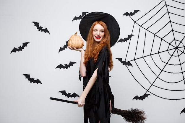 Portrait of beautiful caucasian witch holding pumpkin for celebrating halloween