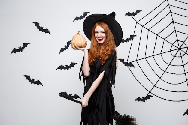 Portrait of beautiful caucasian witch holding pumpkin for celebrating halloween