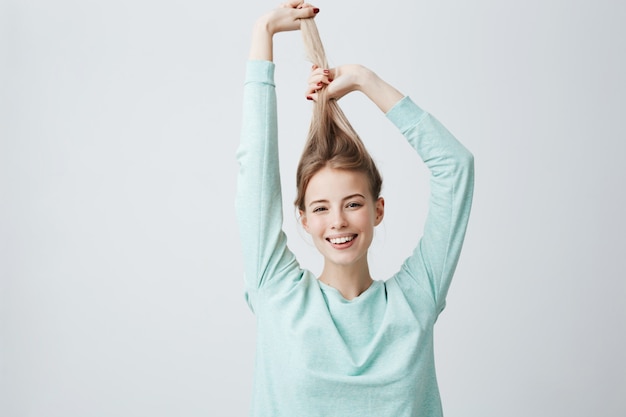 Portrait of beautiful Caucasian woman in light blue shirt, playing with long blonde hair.