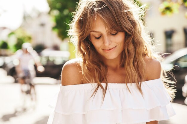 Portrait of beautiful cute blond teenager model with no makeup in summer hipster white dress clothes posing on the street background. Closed eyes