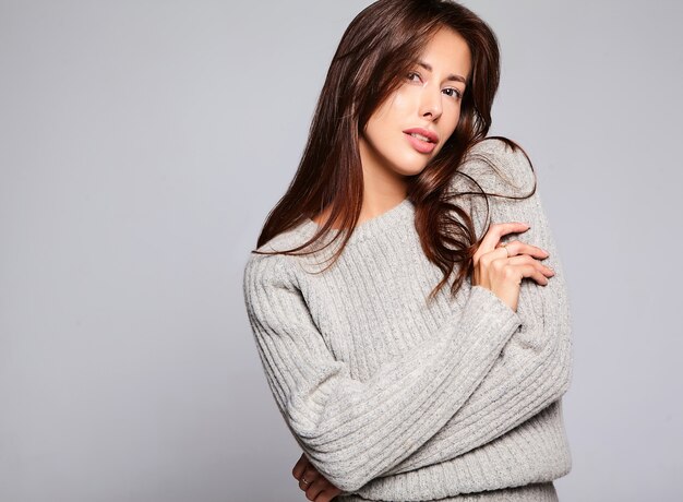 Portrait of beautiful cute brunette woman model in casual autumn gray sweater clothes with no makeup isolated on gray