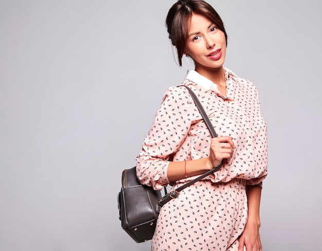 Portrait of beautiful cute brunette woman model in casual summer clothes with no makeup isolated on gray wall with handbag