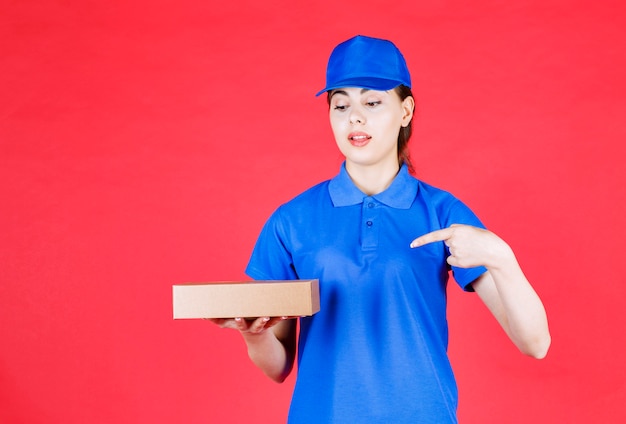 Portrait of beautiful deliverywoman pointing at carton box over red wall.