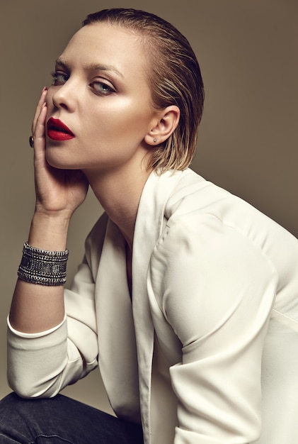 Портрет красивой модной стильной модели брюнетки с вечерним макияжем и красными губами в белой куртке