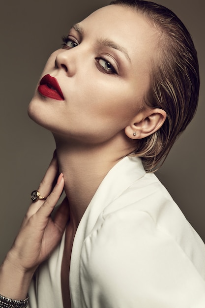 Portrait of beautiful fashion stylish brunette woman model with evening makeup and red lips in white jacket