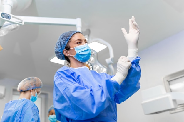 Free photo portrait of beautiful female doctor surgeon putting on medical gloves standing in operation room surgeon at modern operating room