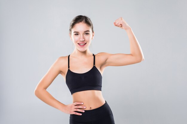 Portrait of a beautiful fitness woman showing her biceps on a white wall