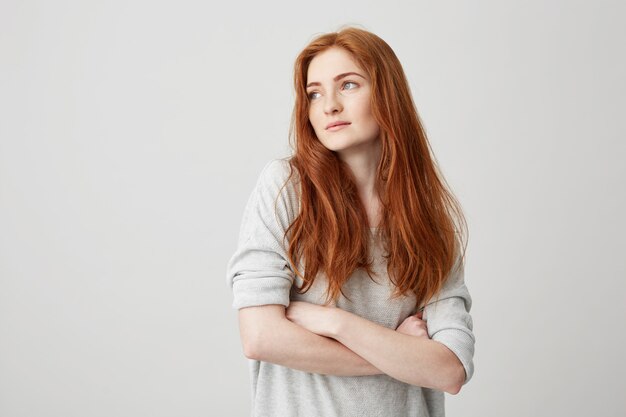 Portrait of beautiful ginger girl with freckles looking in side with crossed arms .