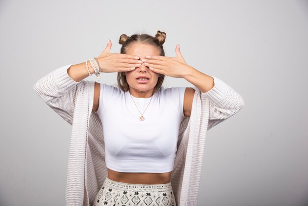 Portrait of beautiful girl covering her eyes on gray background.