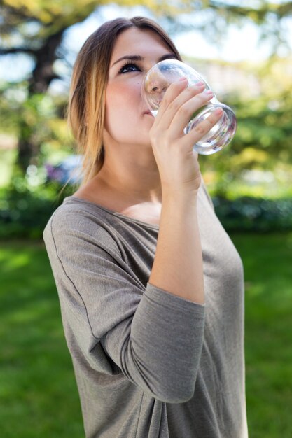 Портрет красивой девушки питьевой воды стекла в зеленый парк.