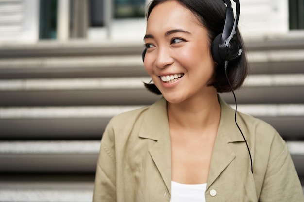 Free photo portrait of beautiful girl in earphones listening music smiling and walking in city centre