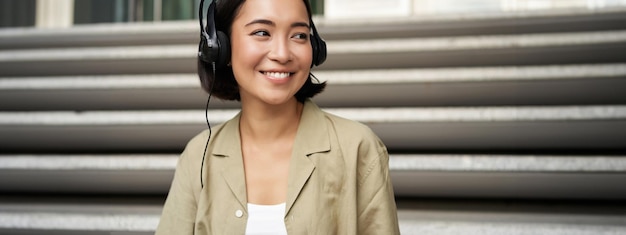 Foto gratuita ritratto di bella ragazza in auricolari che ascolta musica che sorride e che cammina nel centro urbano