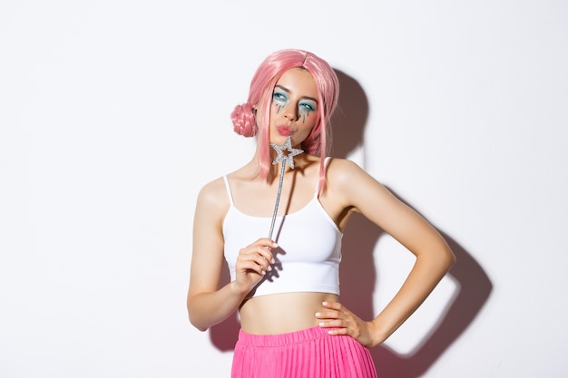 Free photo portrait of beautiful girl in fairy costume looking thoughtful, holding magic wand and wearing pink wig, standing, celebrating halloween.