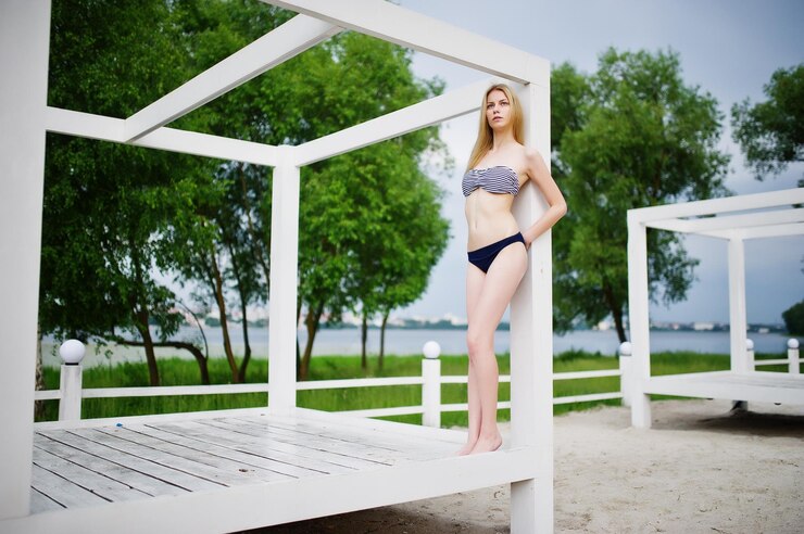 Free Photo portrait of a beautiful girl model standing and posing on a white wooden gazebo next to the lake