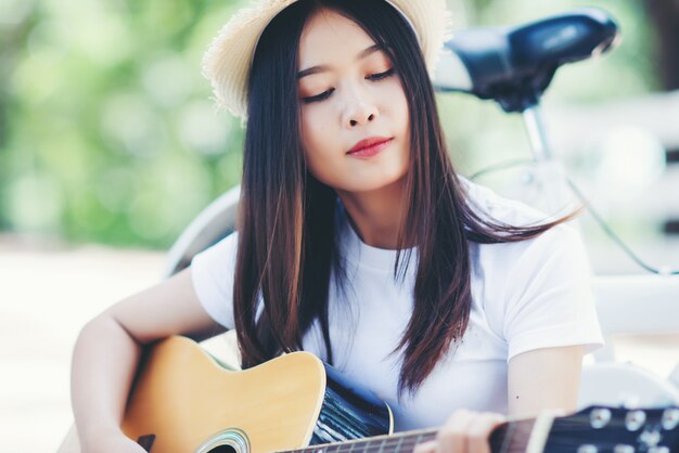 Portrait of beautiful girl playing the guitar with bike at nature