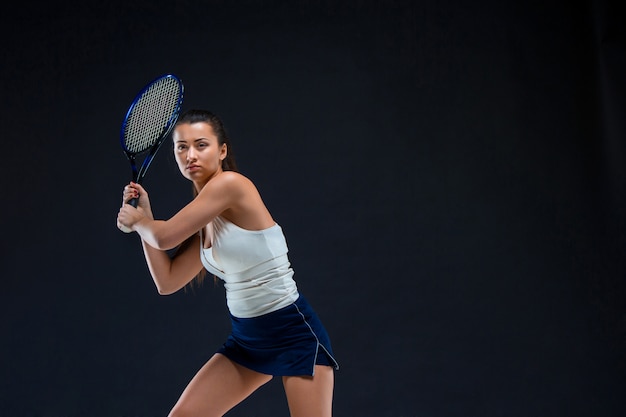 Portrait of beautiful girl tennis player with a racket on dark wall