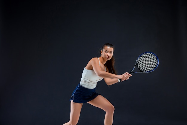 Portrait of beautiful girl tennis player with a racket on dark wall