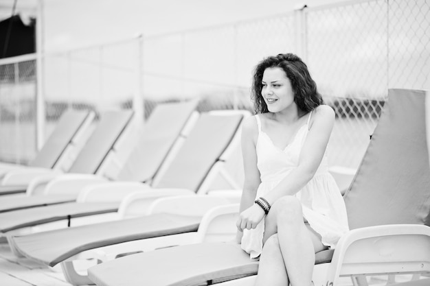 Portrait of a beautiful girl in white summer dress sitting on a lounger Black and white photo