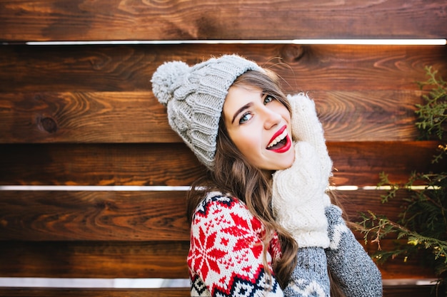 세로 니트 모자와 장갑 나무에 긴 머리와 붉은 입술으로 아름 다운 여자. 그녀는 웃고있다.