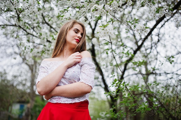 Portrait of beautiful girl with red lips at spring blossom garden wear on red dress and white blouse