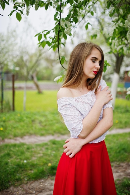 봄 꽃 정원에서 붉은 입술을 가진 아름다운 소녀의 초상화는 빨간 드레스와 흰 블라우스를 입는다