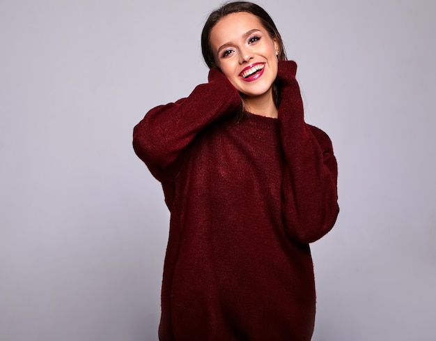 Portrait of beautiful happy cute brunette woman model in casual warm red sweater clothes isolated on gray with evening makeup and colorful lips