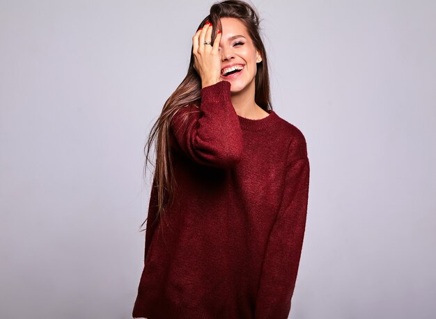 Portrait of beautiful happy cute brunette woman model in casual warm red sweater clothes isolated on gray with evening makeup and colorful lips