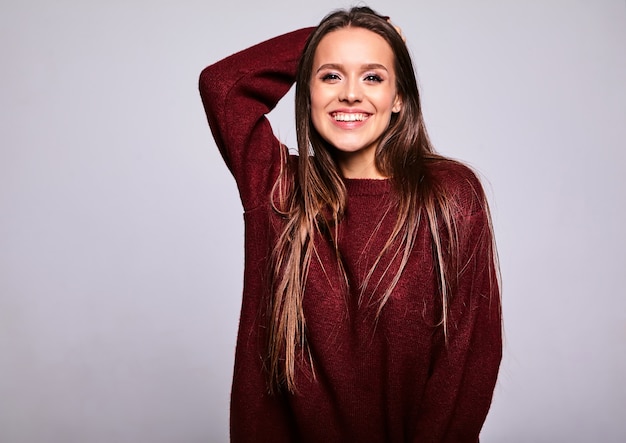 Portrait of beautiful happy cute brunette woman model in casual warm red sweater clothes isolated on gray with evening makeup and colorful lips